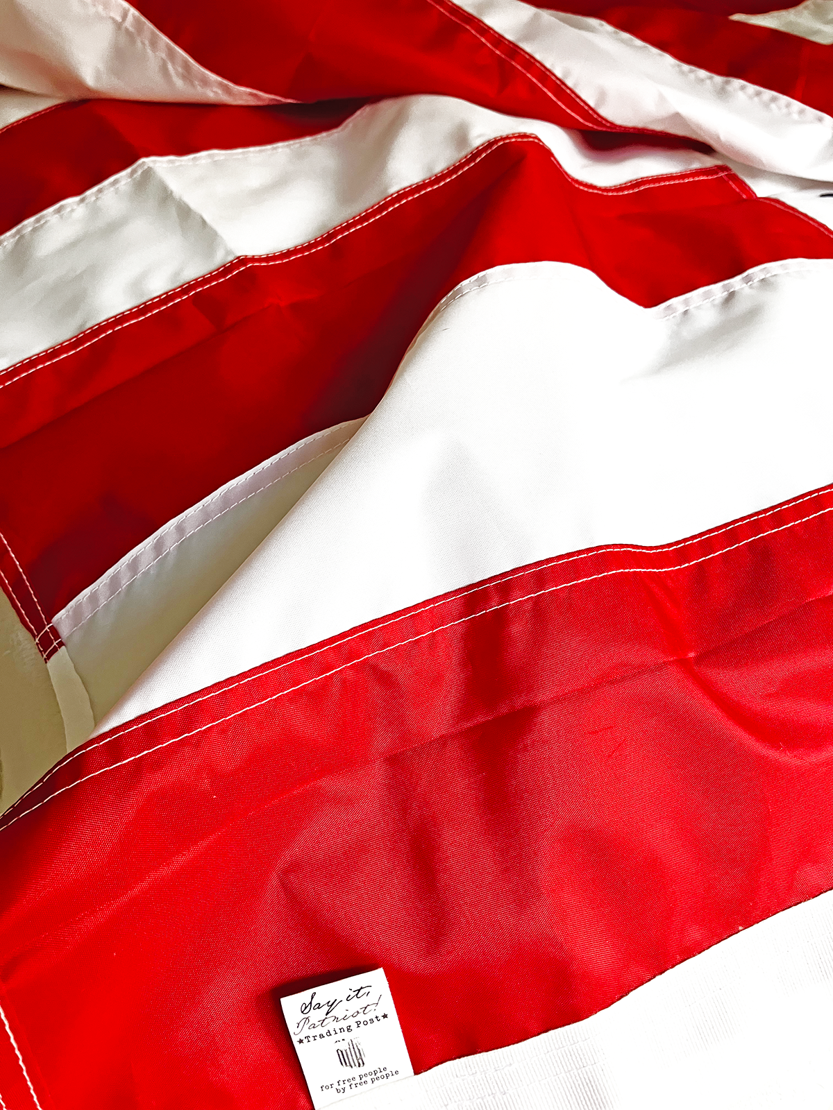 Image of red and white stripes on a flag with Say It, Patriot Logo on tag